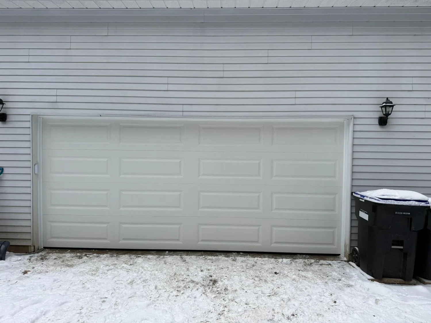 White sectional garage door with snow on the driveway